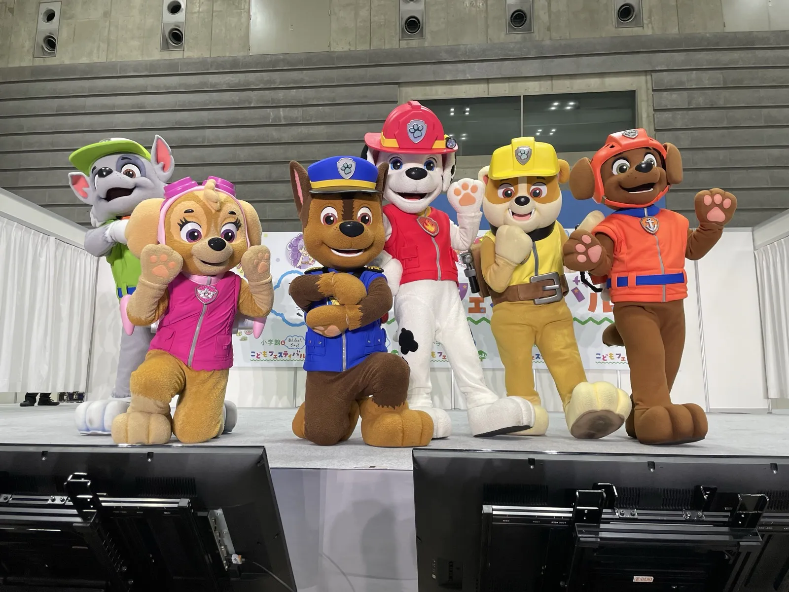 ステージに並んでポーズをとるロッキー、スカイ、チェイス、マーシャル、ラブル、ズーマの着ぐるみ。手前に最前列から見たステージ前のモニターが写っている